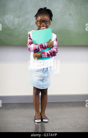 Portrait of happy schoolgirl holding file in classroom Stock Photo