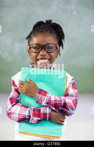 Portrait of happy schoolgirl holding file in classroom Stock Photo