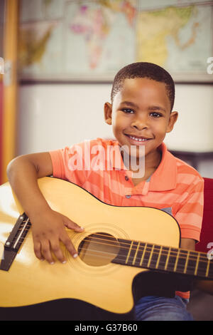 Portrait of smiling schoolboy playing guitar in classroom Stock Photo