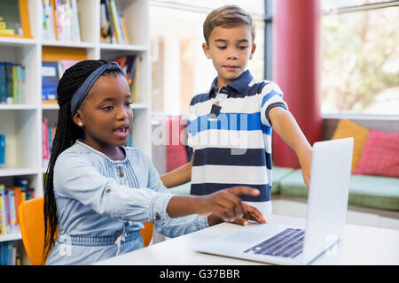 School kids using a laptop in library Stock Photo