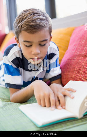 Schoolboy lying on sofa and reading book Stock Photo
