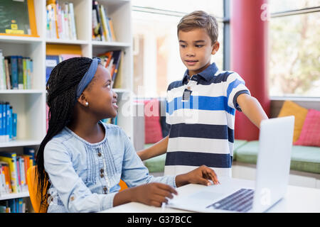 School kids using a laptop in library Stock Photo