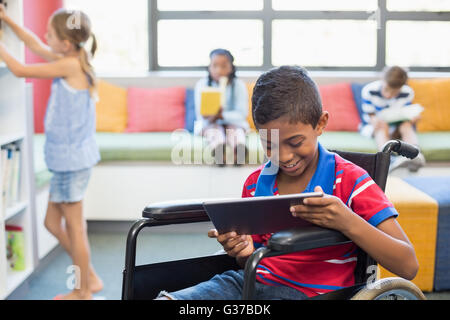 Disabled schoolboy on wheelchair using digital tablet in library Stock Photo