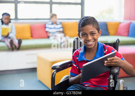 Disabled schoolboy on wheelchair using digital tablet in library Stock Photo