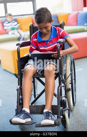 Disabled schoolboy on wheelchair using digital tablet in library Stock Photo