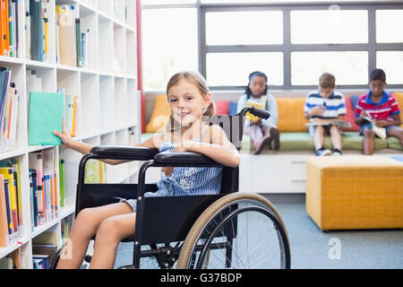 Disabled school girl selecting a book from bookshelf in library Stock Photo