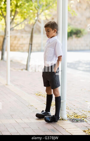 Thoughtful schoolboy leaning on pole with hands in pocket Stock Photo