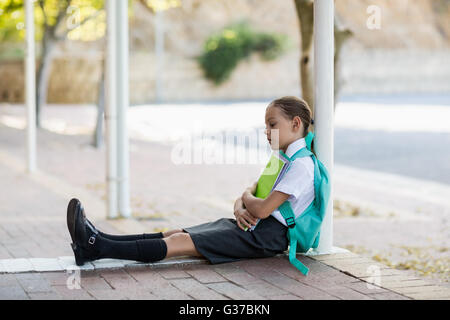 Thoughtful schoolgirl sitting alone in corridor Stock Photo