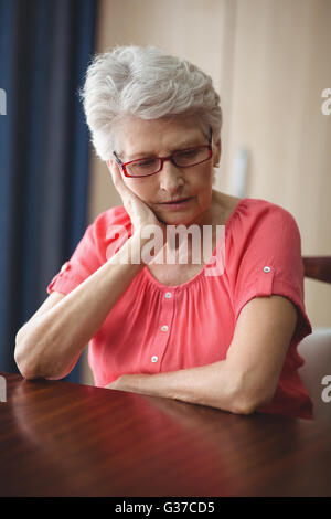 Sad senior woman sitting at a table Stock Photo