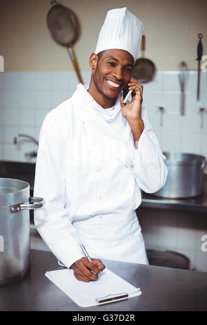 Chef writing on clipboard while talking on phone Stock Photo