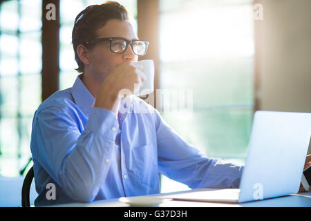 Man drinking a coffee while using a laptop Stock Photo
