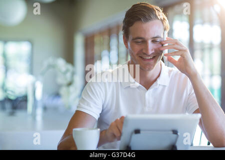 Smiling man talking on mobile phone while using digital tablet Stock Photo