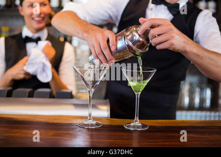Mid section of bartender pouring cocktail into glasses Stock Photo