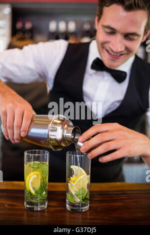 Bartender pouring a drink from a shaker to a glass on bar counter Stock Photo