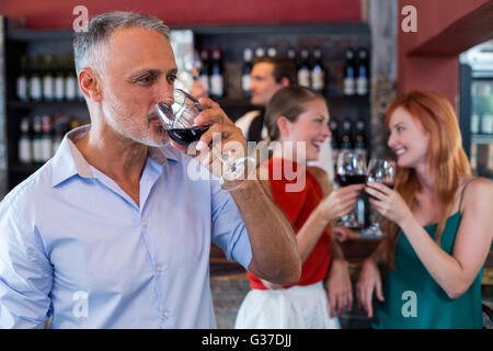 Man drinking red wine while two friends toasting the glasses in background