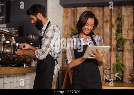 Waitress using a tablet computer and waiter with coffee machine Stock Photo