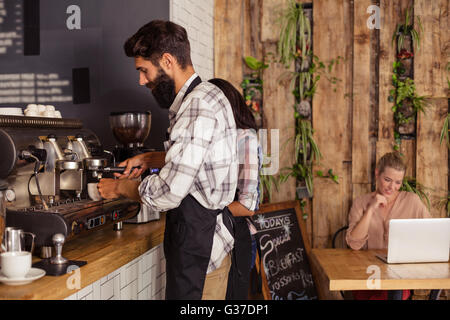 Waiters using a coffee machine and customer on a laptop Stock Photo