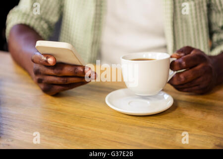 Hand holding a cup of coffee while using a smartphone Stock Photo