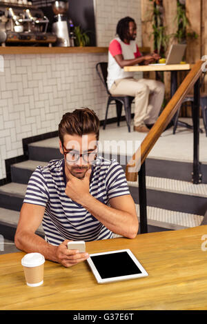 Young man sitting at table using a smartphone Stock Photo