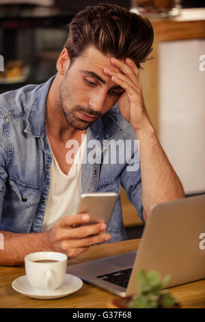 Unsmiling hipster man holding up his head while using smartphone Stock Photo
