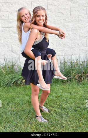 Little blond girl getting a piggyback ride from her teenage sister. Stock Photo
