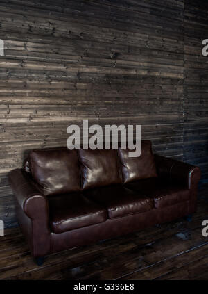 vintage brown leather sofa on a wooden wall and floor Stock Photo