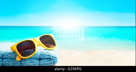 Summer accessory item. Yellow sunglass and blue towel on the beach. Stock Photo