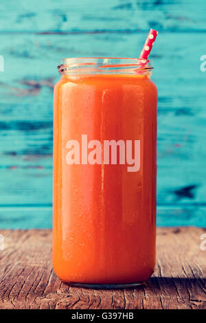 closeup of an orange detox smoothie served in a glass jar with a red drinking straw patterned with white dots, on a rustic woode Stock Photo