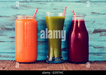 closeup of three different fresh smoothies served in a glass, a glass jar and a glass bottle with red drinking straws patterned Stock Photo