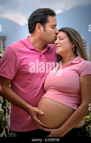 Portrait of a happy young couple expecting a new baby, hugging outdoors. Husband is kissing his wife. Outdoors. Stock Photo