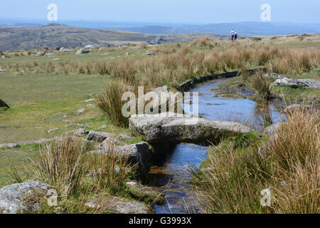 Clapper Bridge over Longash Leat, with two people in the distance walking towards the Merrivale Standing Stone, Dartmoor, Devon Stock Photo