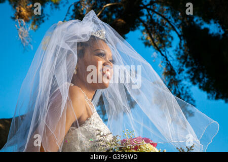 A stunning African American bride looks off to the distance with her veil over her face and blowing in the wind. Stock Photo