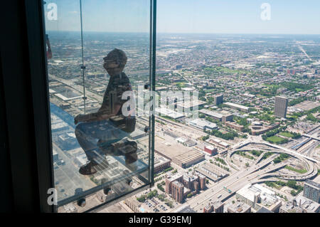 A man has his photograph taken on the glass balcony to the observation deck of the Willis Tower, with an aerial view of Chicago. Stock Photo