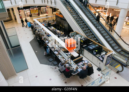 People eating Japanese food at a branch of Yo! Sushi in shopping mall in Bromley with bowls of food passing on conveyor belt. Stock Photo