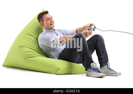 Joyful young man playing video games seated on a green beanbag isolated on white background Stock Photo