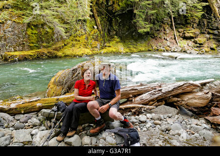 41,795.08221 Man and woman sitting on a rock in a canyon beside the fast flowing Chinook River Stock Photo