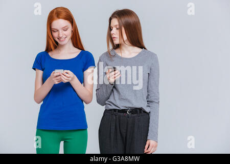 Two smiling depressed young women standing and using cell phones Stock Photo
