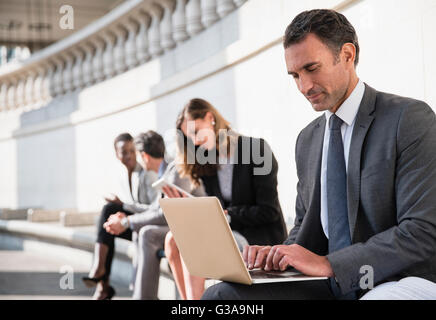 Corporate businessman using laptop on bench outdoors Stock Photo
