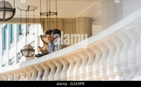 Corporate businessman and businesswoman with coffee and cell phone at railing Stock Photo