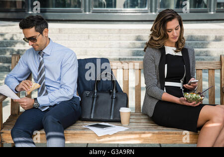Corporate businessman and businessman working and eating lunch on bench Stock Photo