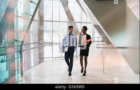 Corporate businessman and businesswoman walking and talking in modern office lobby Stock Photo
