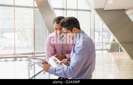 Corporate businessmen reviewing paperwork in modern office lobby Stock Photo