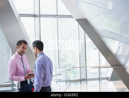 Corporate businessmen with digital tablet talking in modern office lobby Stock Photo