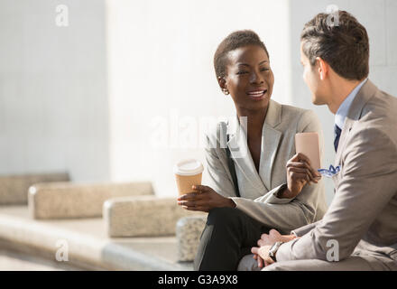 Corporate businessman and businesswoman with coffee and cell phone talking on bench Stock Photo