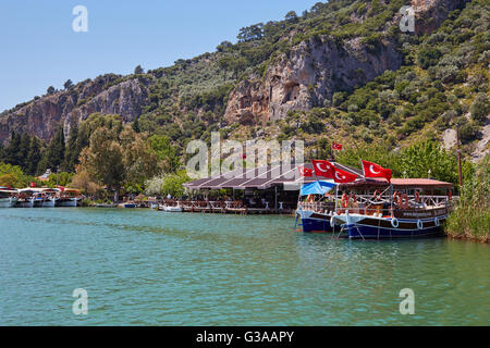 Boats on the Dalyan  Çay river with the Lycian tombs in the cliffs above, Turkey. Stock Photo