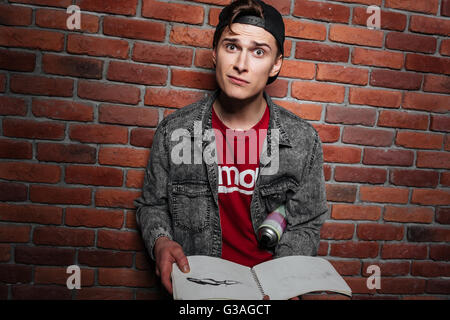 Graffiti man in cap holding sketchbook isolated over red brick wall Stock Photo