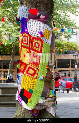 The trunk of a tree covered with a patchwork of coloured bright knitted patterns, in the Flag Market, Preston, Lancashire, UK Stock Photo