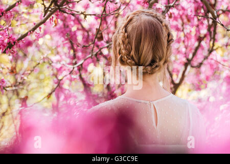 Back view of blonde young woman standing in spring blooming garden Stock Photo