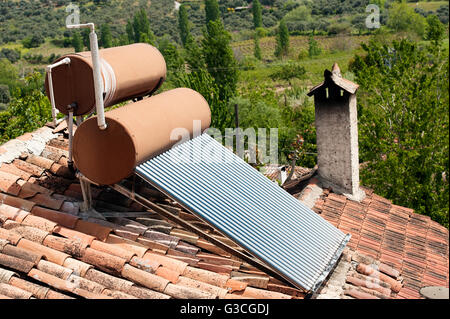 A solar water heating system is installed on the tiled roof of a rural home, with two cylindrical water tanks and solar tubes absorbing sunlight. Stock Photo