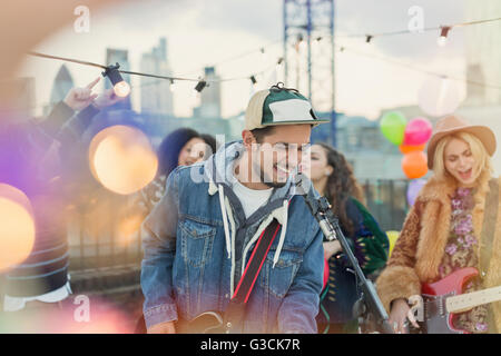 Enthusiastic musician playing guitar and singing at rooftop party Stock Photo